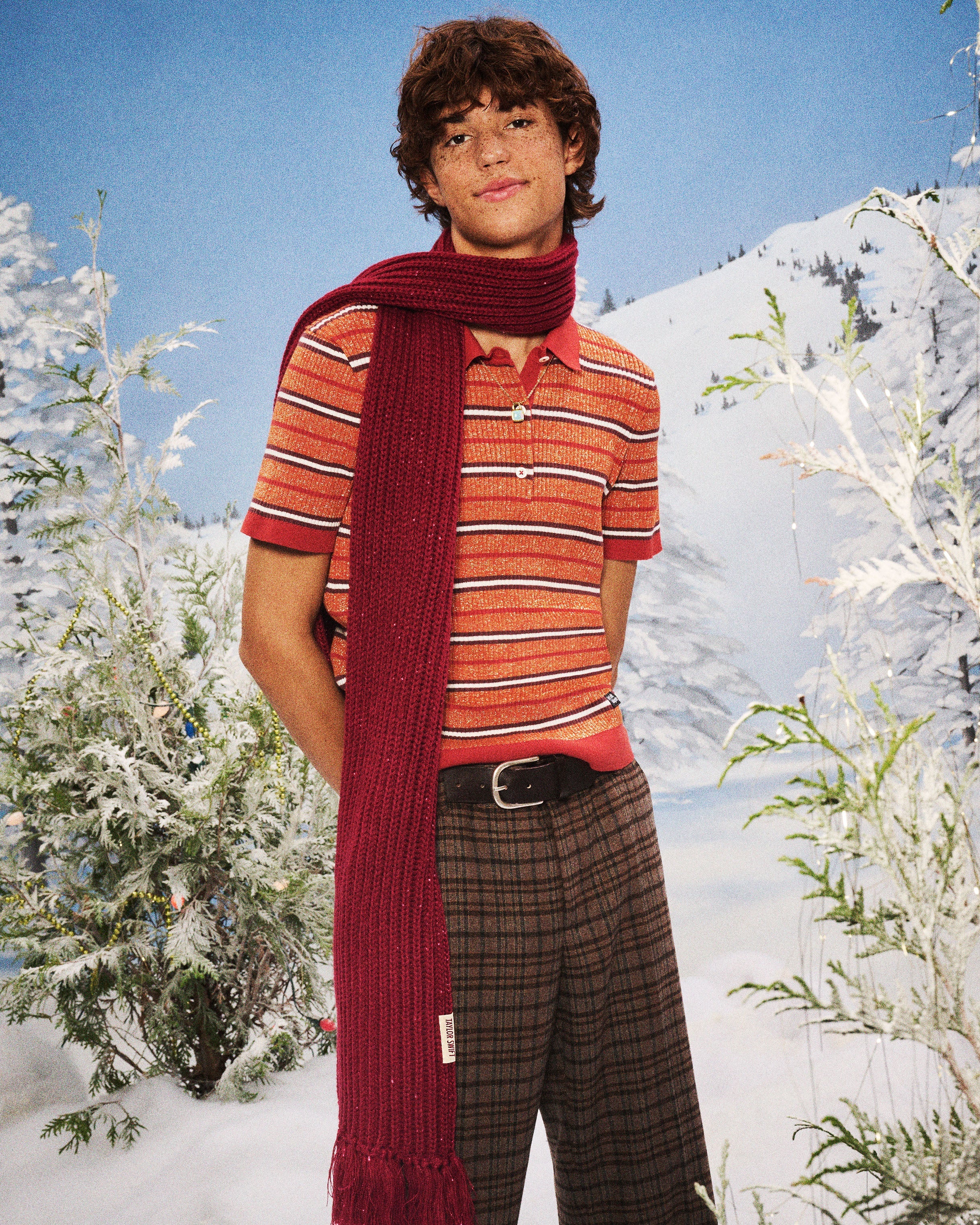 Person wearing a red striped shirt and plaid pants with a long red scarf in a snowy landscape.